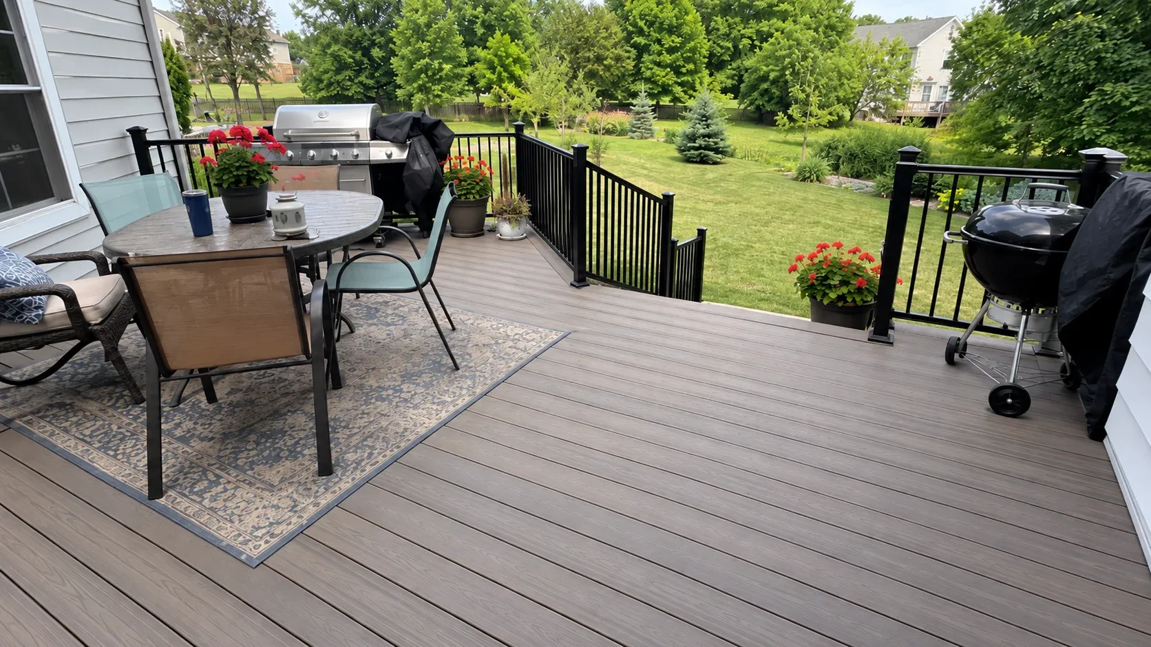 A composite deck with black aluminium railings at sunset, steps rising to an upper level beside the house